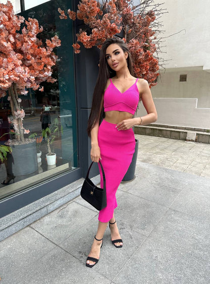 Woman in a bright pink outfit standing outdoors near a building entrance.