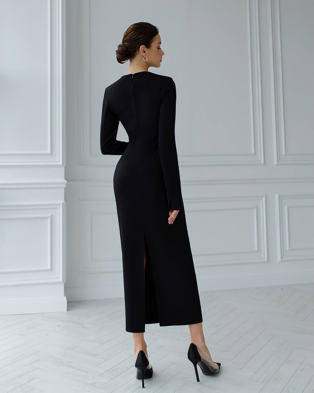 Woman wearing a black dress with a high slit in a white room