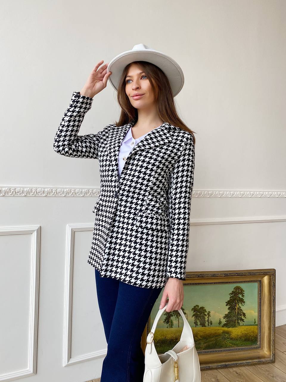 Woman wearing a black and white checkered blazer with a white hat indoors.