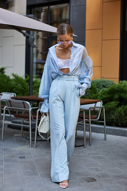 Woman in light blue outfit walking outdoors near a building with tables and chairs.