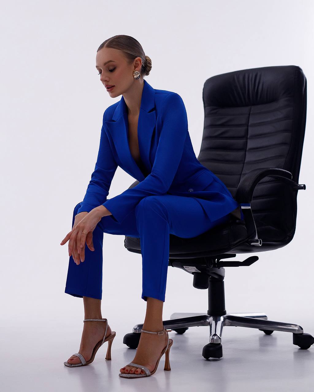 Woman in a blue suit sitting on a black office chair against a white background