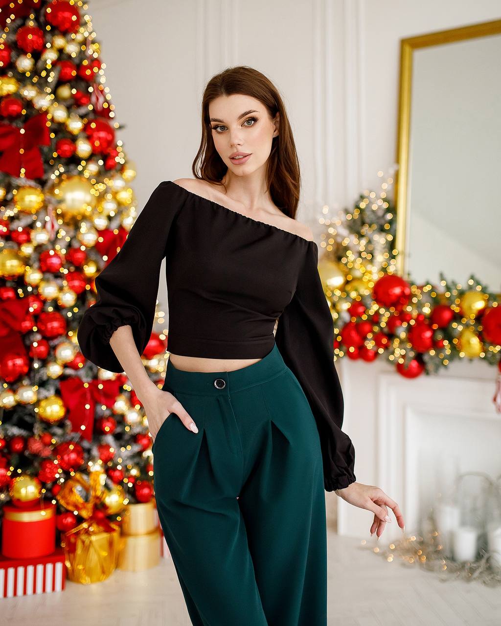 Woman posing in a stylish outfit with a decorated Christmas tree in the background