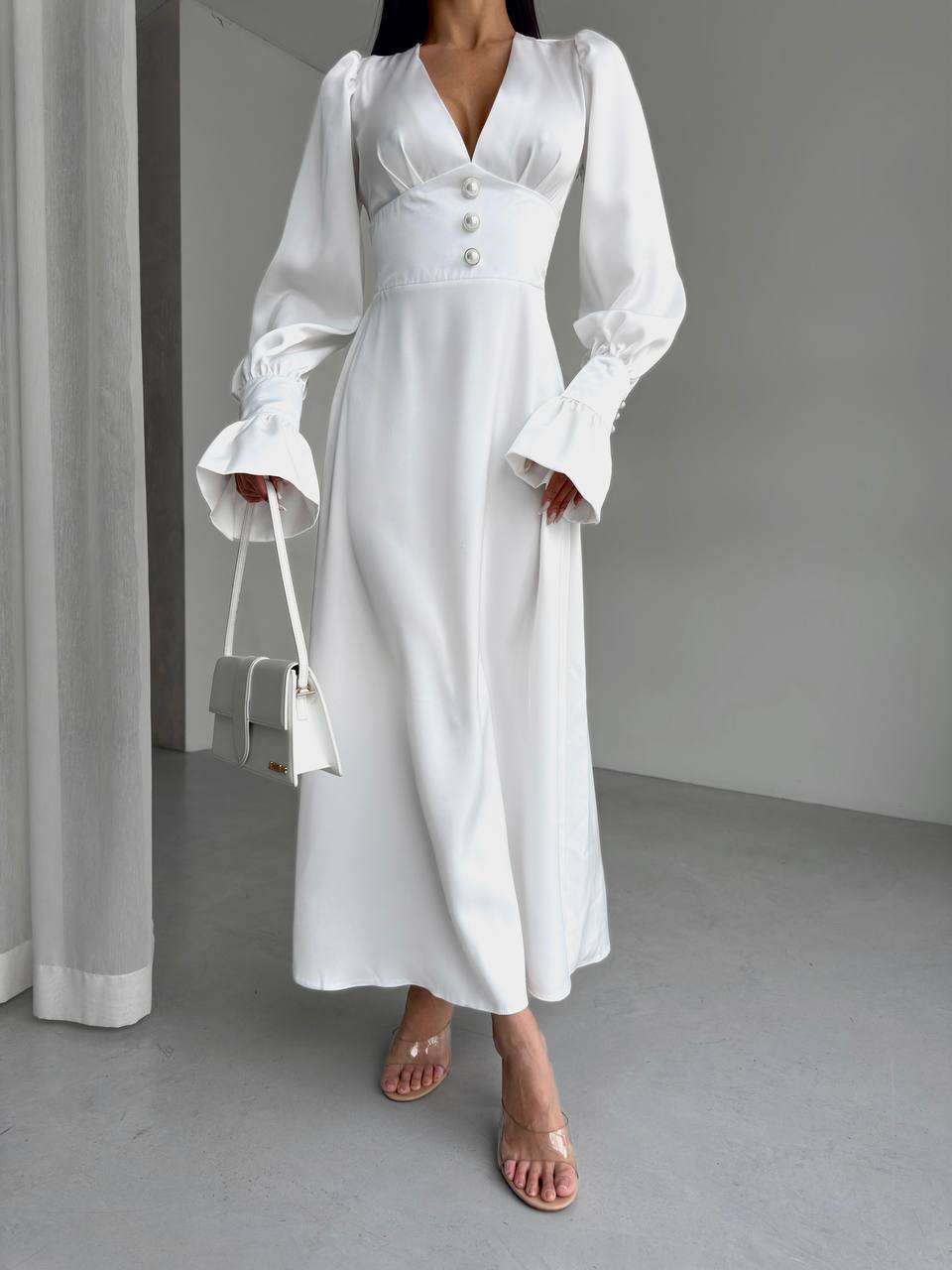 Woman wearing a white dress holding a white handbag in a minimalistic setting