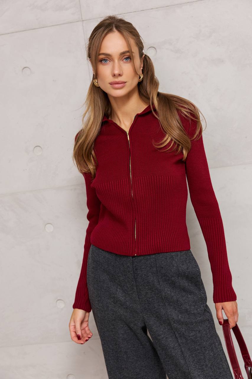 Woman wearing a red ribbed sweater and gray pants against a light gray background