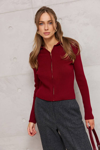 Woman wearing a red ribbed sweater and gray pants against a light gray background