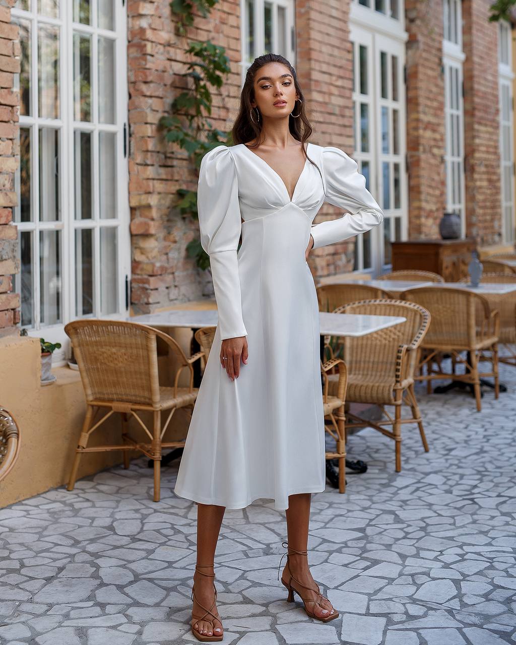 Woman in a white dress standing in an outdoor setting with tables and chairs.