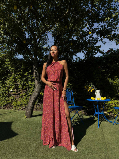 Woman in a red dress standing outdoors with greenery and a blue chair in the background