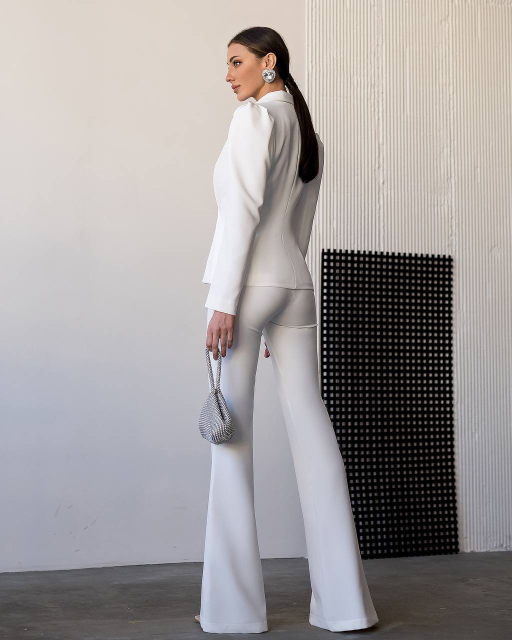 Woman in a white outfit standing against a plain wall.