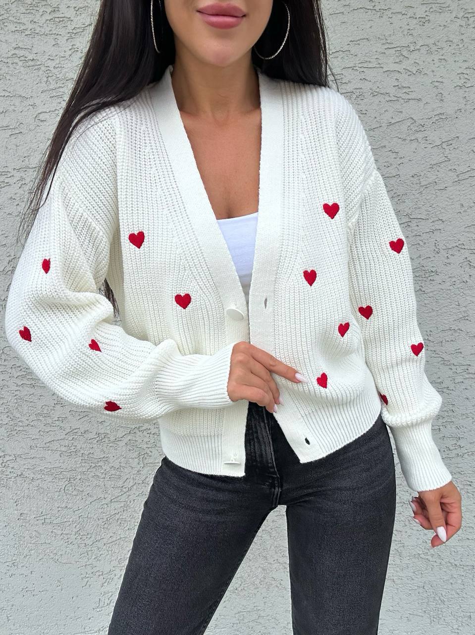 White cardigan with red heart patterns worn by a person against a gray background