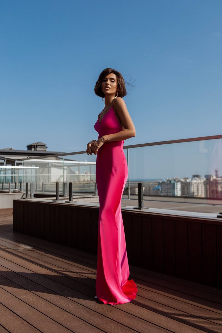 Woman in a pink evening gown standing on a rooftop with a clear blue sky.