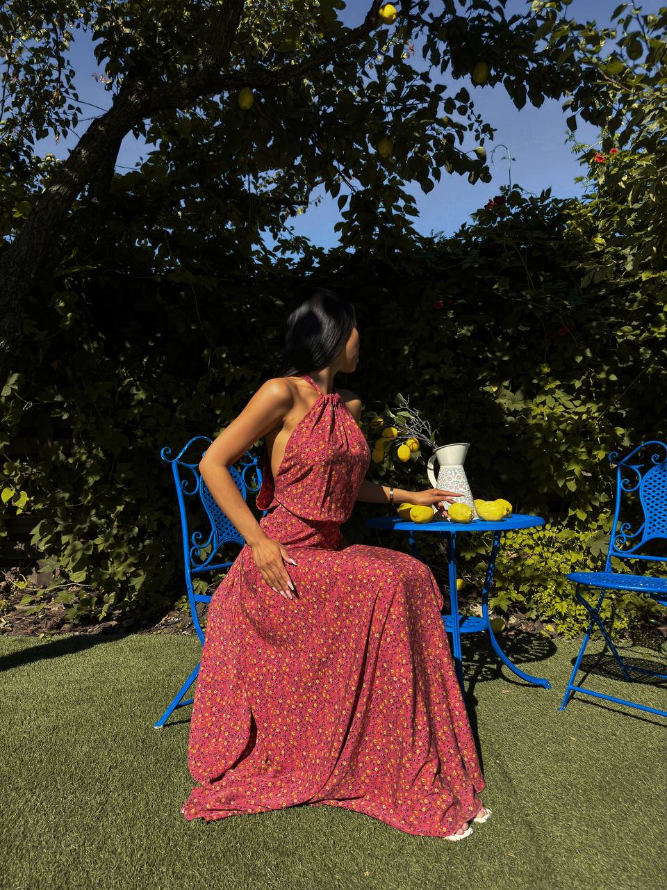 Woman in a red dress sitting outdoors with blue chairs and a table.