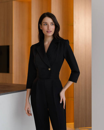 Woman wearing a black suit standing in an indoor setting with wooden walls.