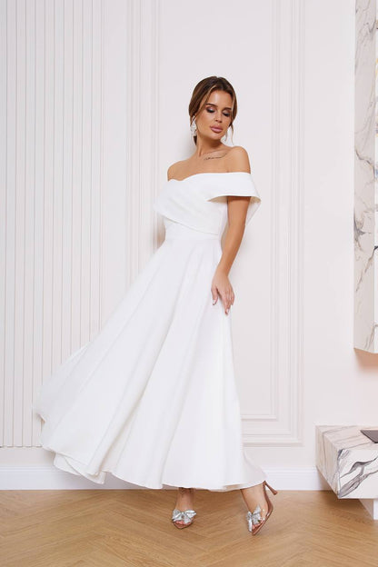 Woman wearing a white off-shoulder dress in a room with light-colored walls.