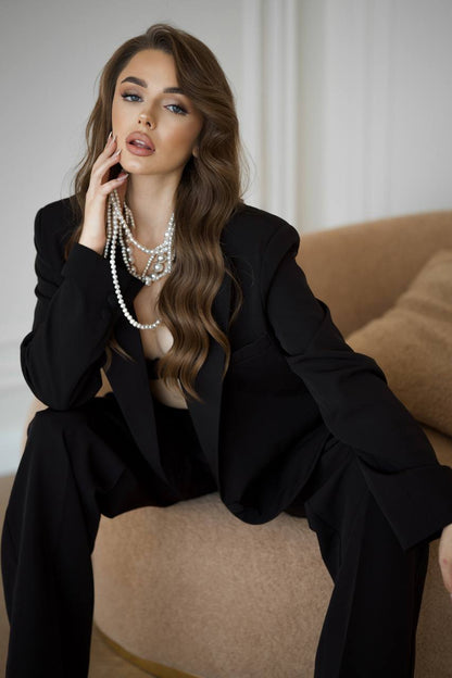 Woman in a black outfit with layered pearl necklaces sitting on a beige couch.