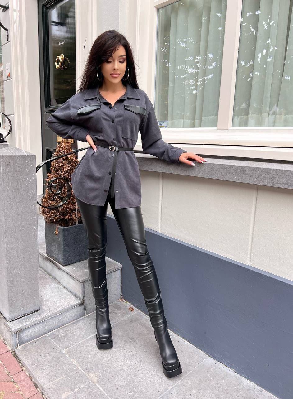 Woman in a gray shirt and black leather pants standing on a sidewalk.