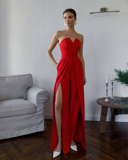 Woman wearing a red strapless gown with a high slit in a room with a gray sofa and wooden table.