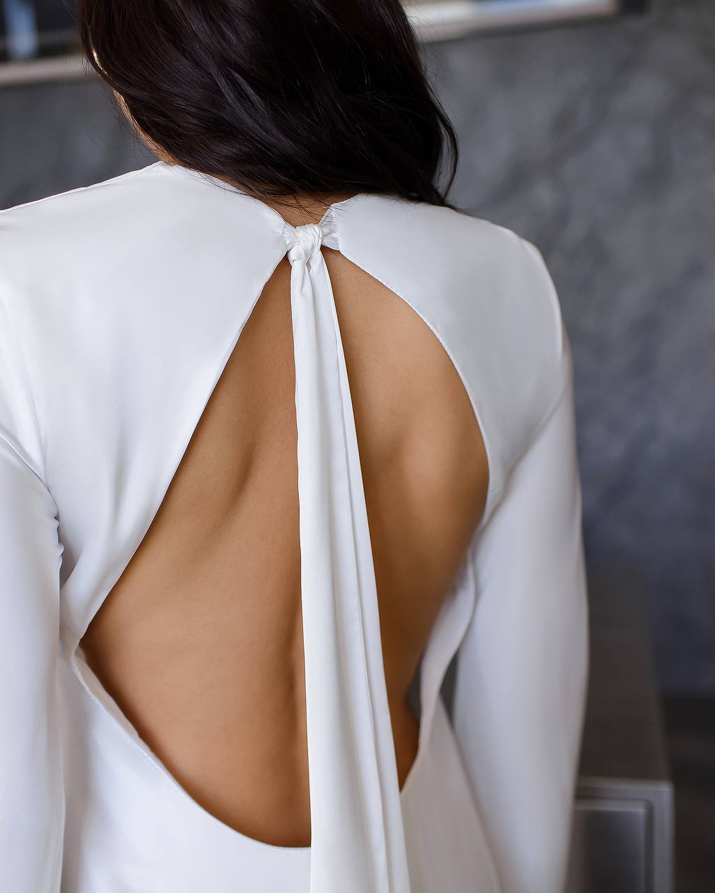 White dress with open back worn by a person, blurred background