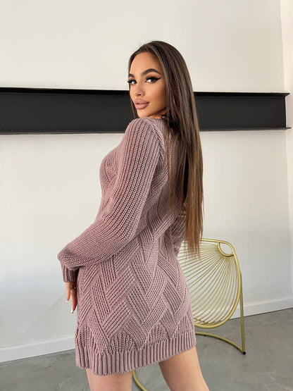 Woman wearing a pink knitted dress standing against a white wall.