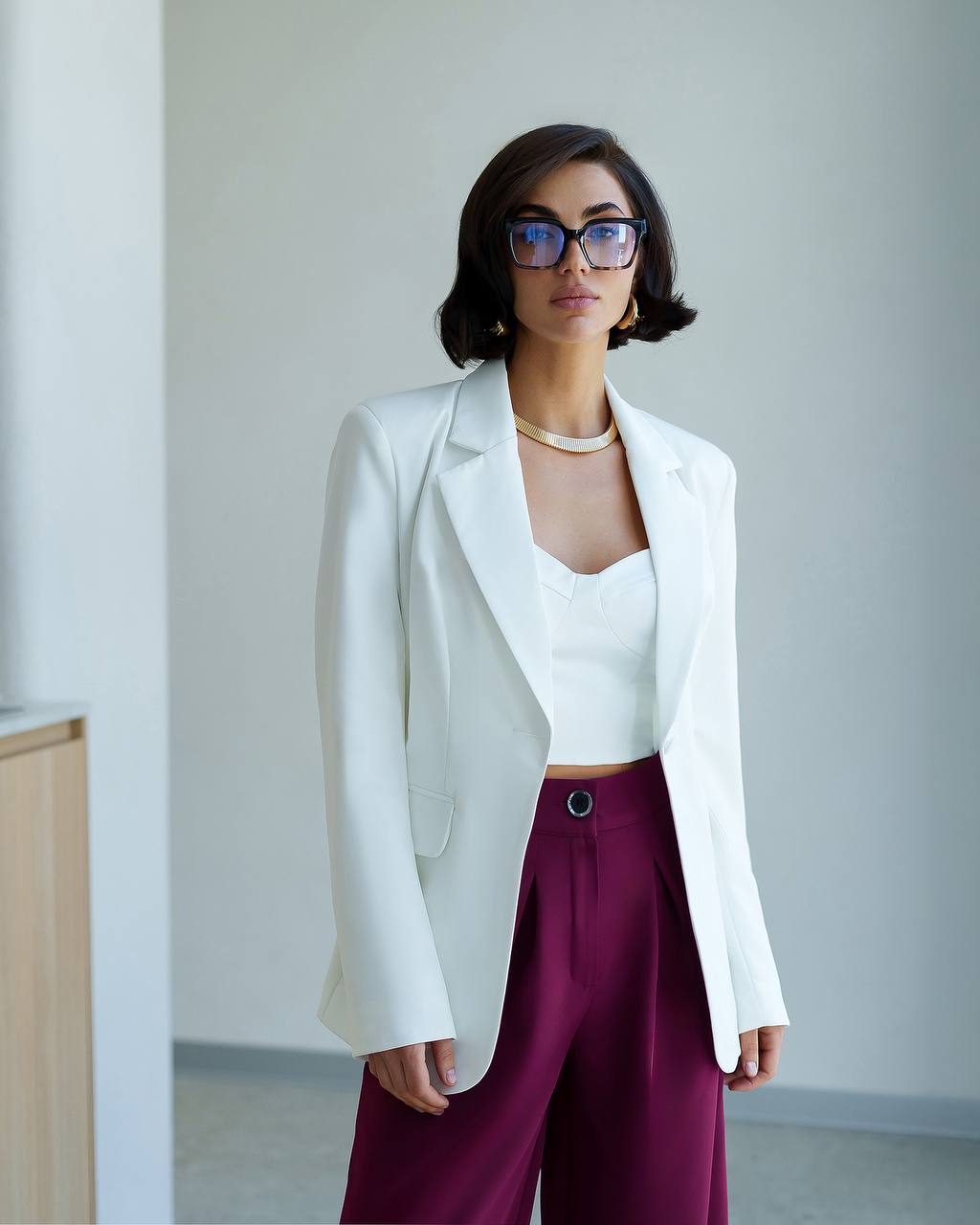 Woman wearing a white blazer and burgundy pants in an indoor setting