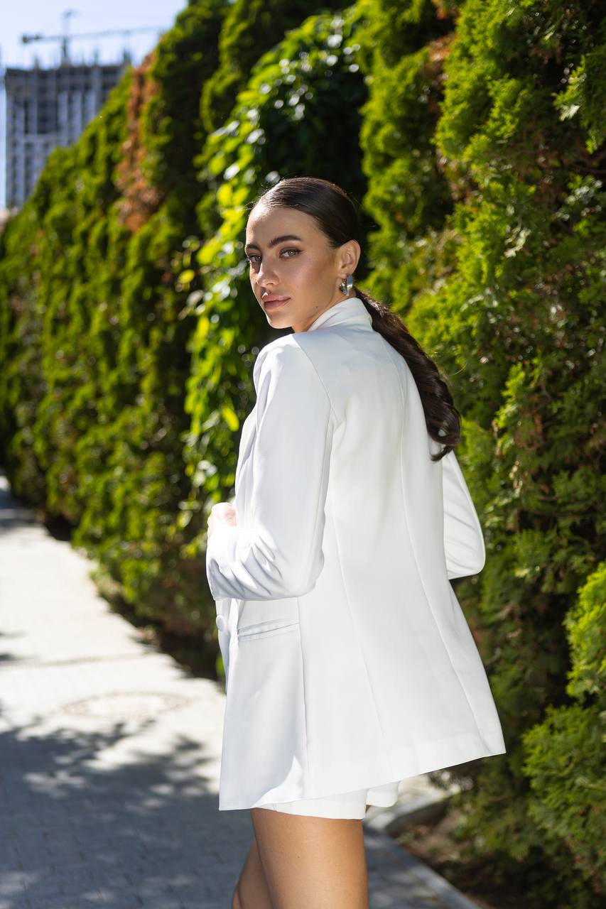 Woman in a white outfit standing against a green hedge
