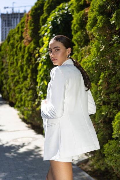 Woman in a white outfit standing against a green hedge