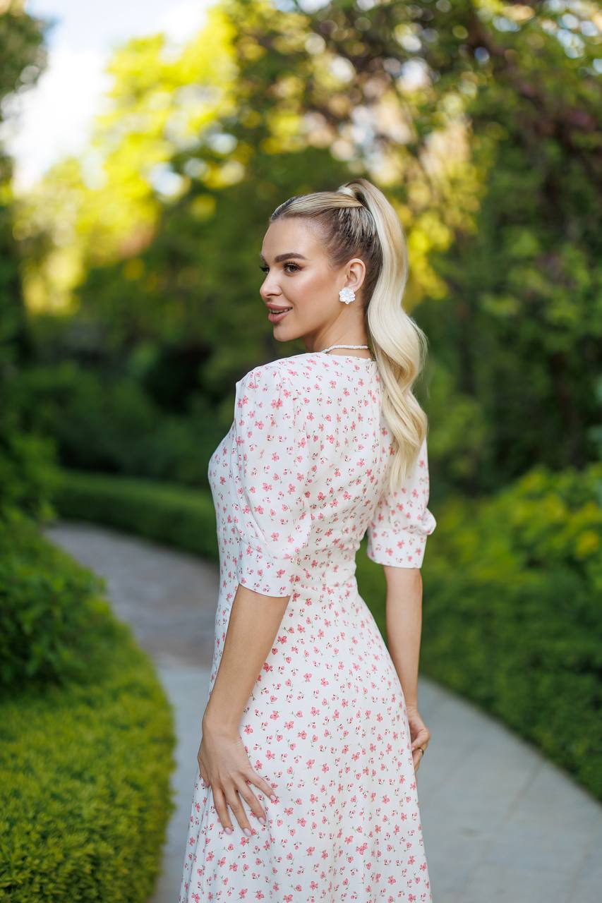 Woman in a white floral dress standing outdoors with greenery in the background