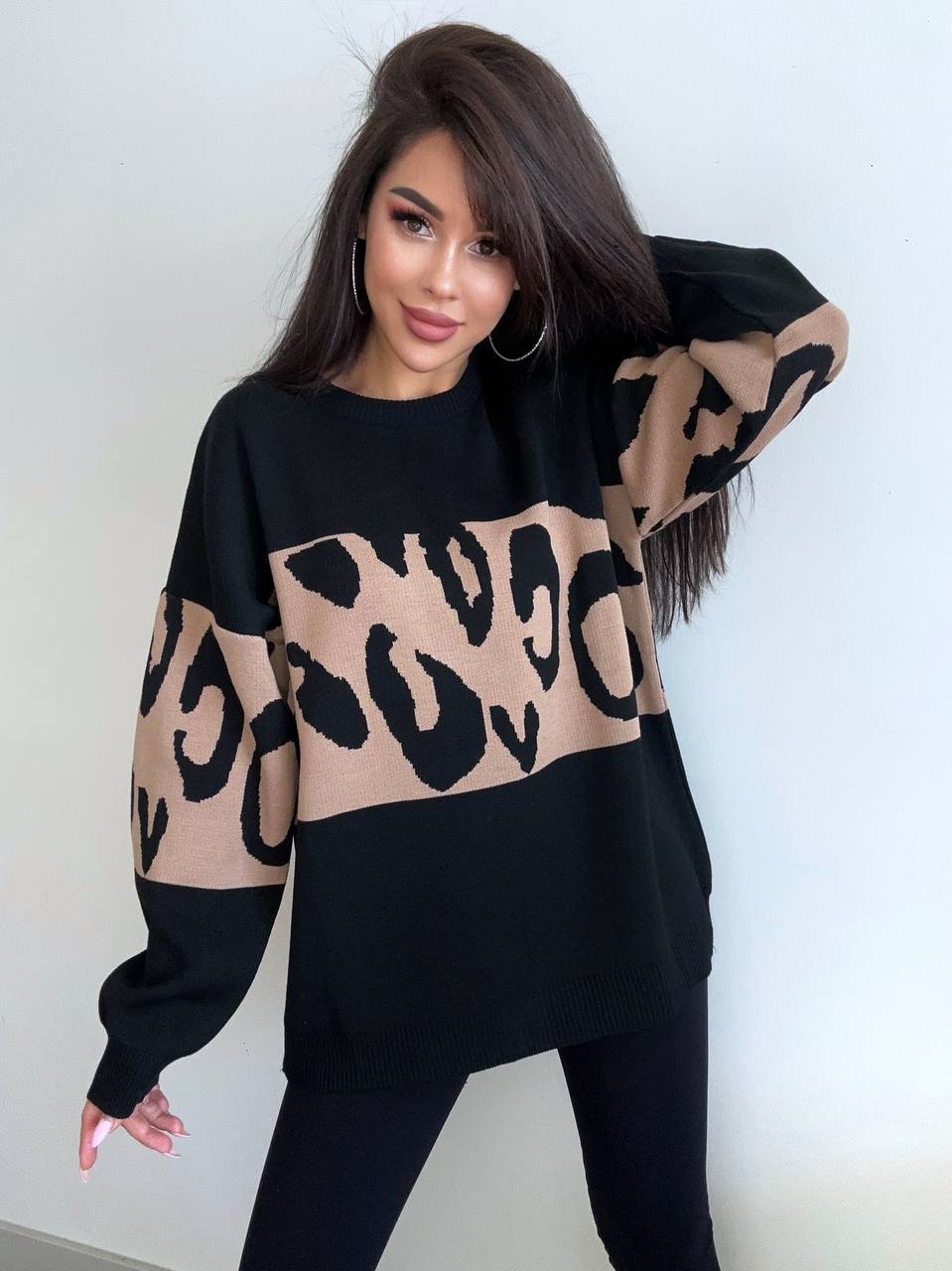 Woman wearing a black and beige leopard print sweater against a white background