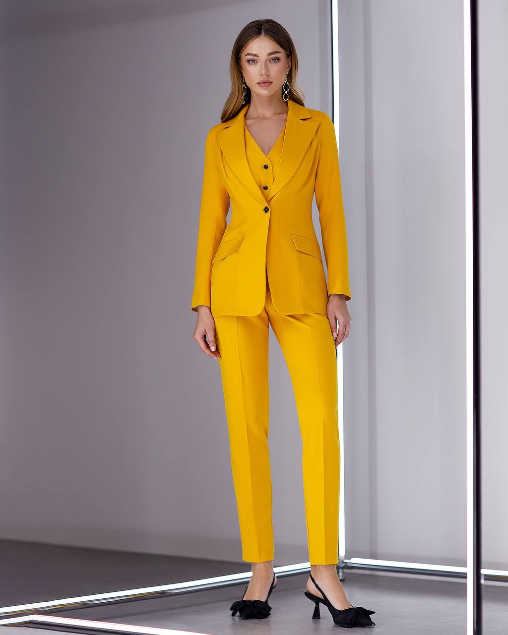 Woman wearing a yellow suit standing against a plain background