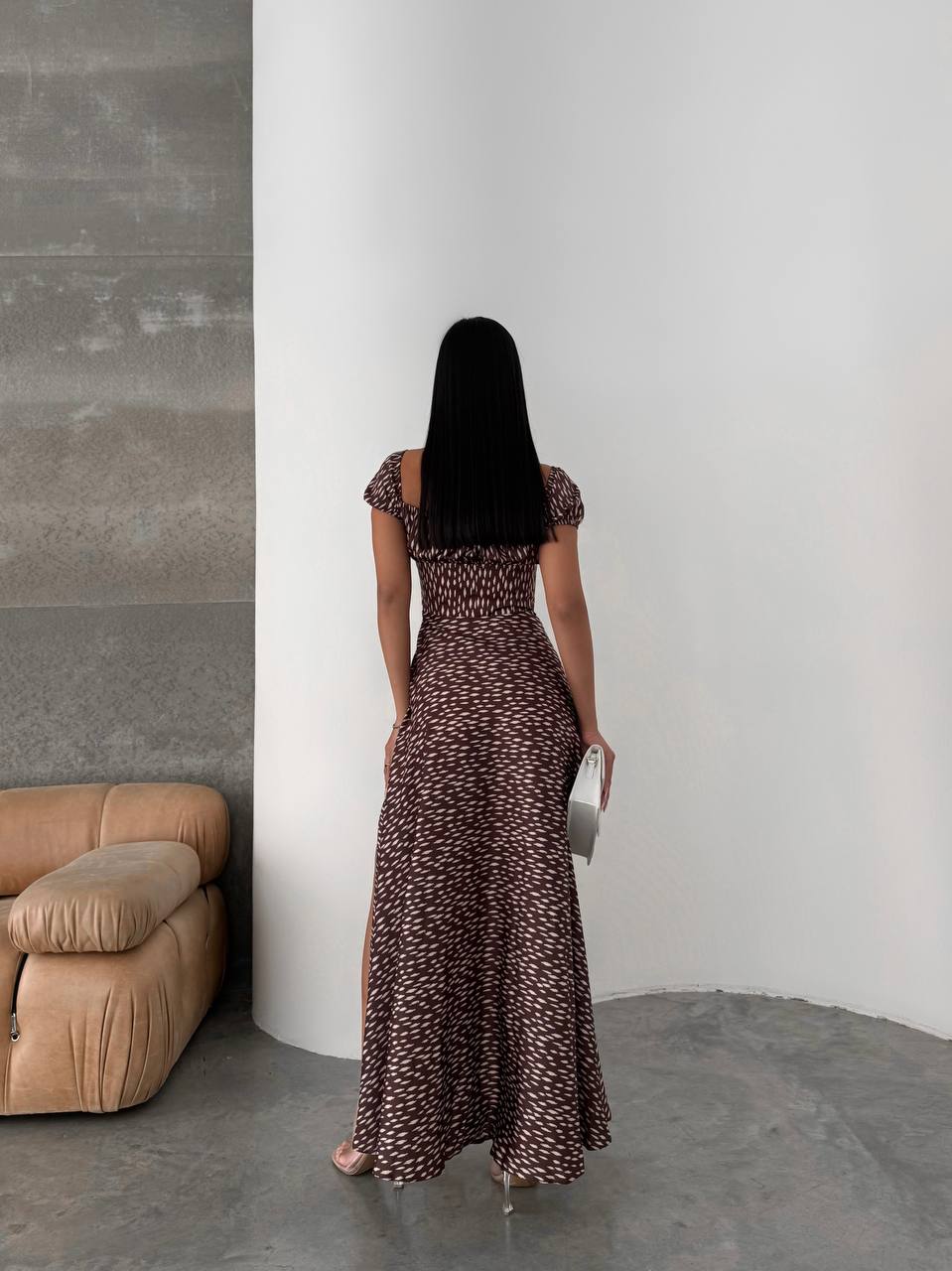 Woman in a long patterned dress standing against a white wall in a minimalistic room.