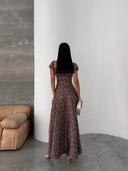 Woman in a long patterned dress standing against a white wall in a minimalistic room.