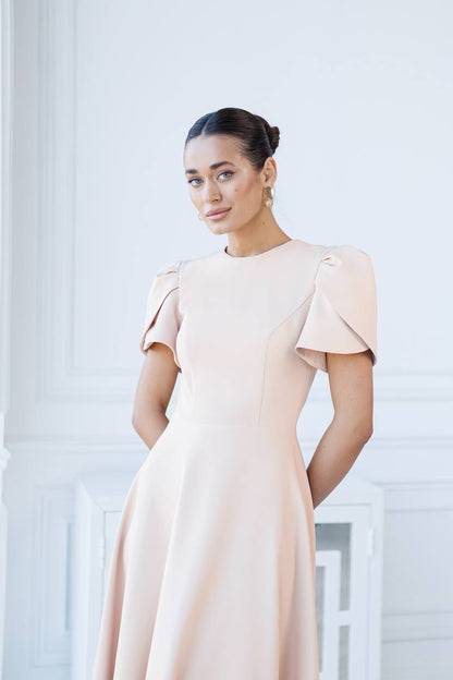 Woman wearing a beige dress with ruffled sleeves against a white background