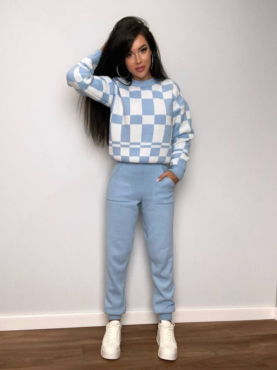 Woman wearing a blue and white checkered outfit against a plain wall.