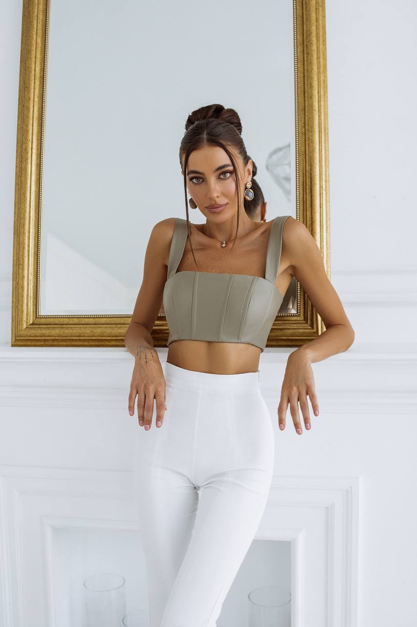 Woman wearing a green crop top and white pants standing in front of a mirror.