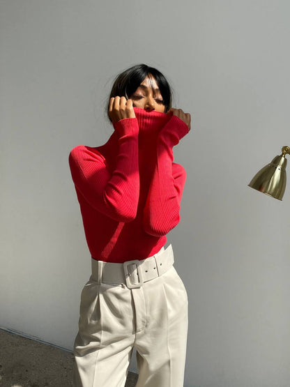 Person wearing a red sweater and beige pants against a plain wall.