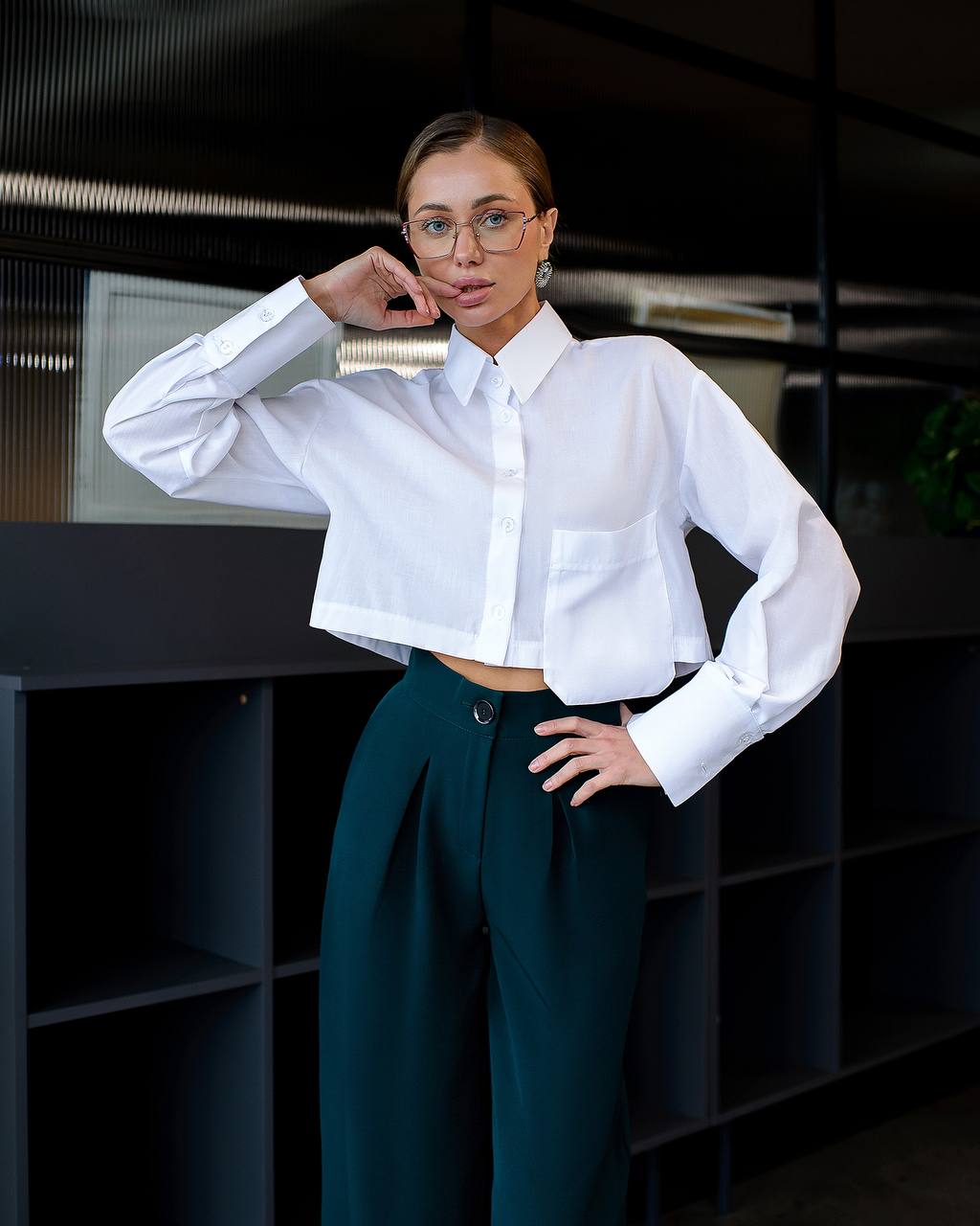 Woman wearing a white shirt and teal pants in an indoor setting