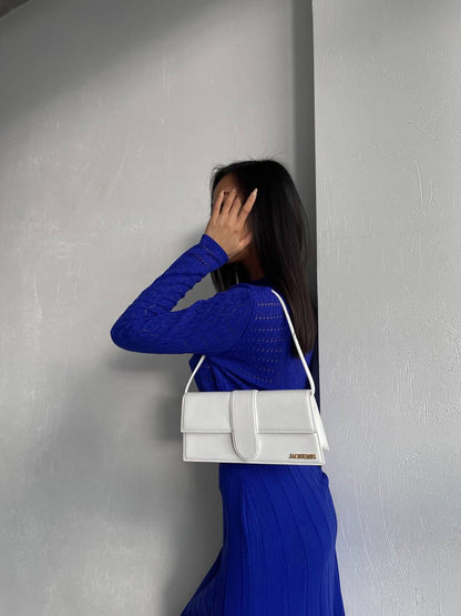 Woman in a blue dress holding a white handbag against a gray wall