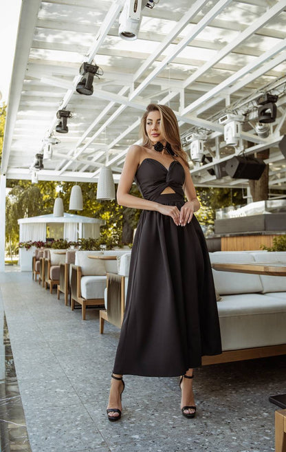 Woman in a black dress standing in an outdoor setting with tables and chairs.