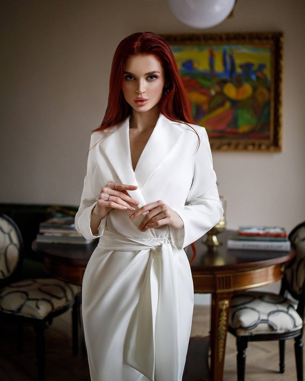 Woman in a white robe standing in a room with a colorful painting on the wall.