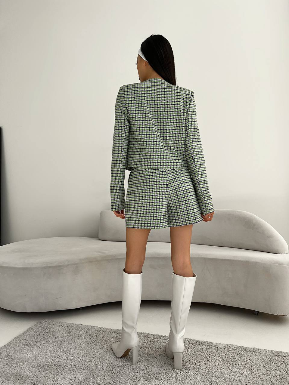 Person wearing a green checkered outfit with white boots in a minimalistic room.