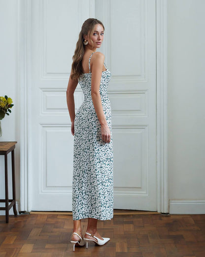 Woman in a floral dress standing in a room with wooden flooring and white walls.