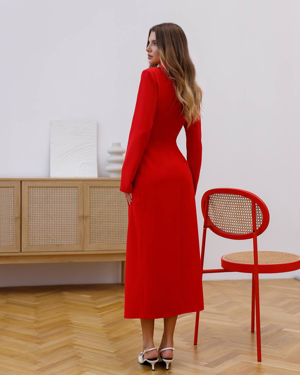 Woman in a red dress standing in a room with a wooden floor and white walls.