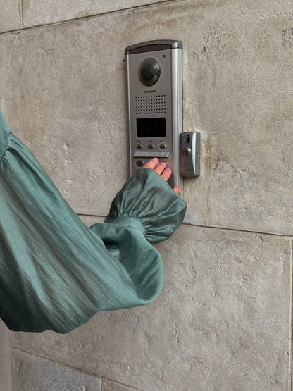Person wearing a green glove pressing a doorbell on a stone wall.