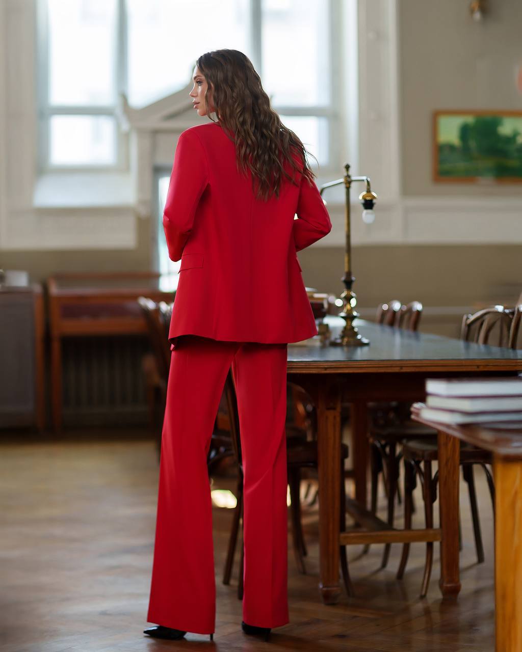 Woman in a red suit standing in a room with wooden tables and chairs.
