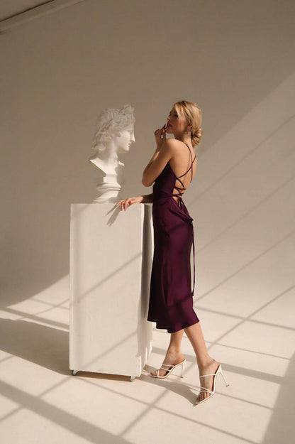 Woman in a purple dress standing next to a white sculpture in a sunlit room