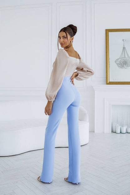 Woman wearing a beige off-shoulder top and light blue pants in a white room.