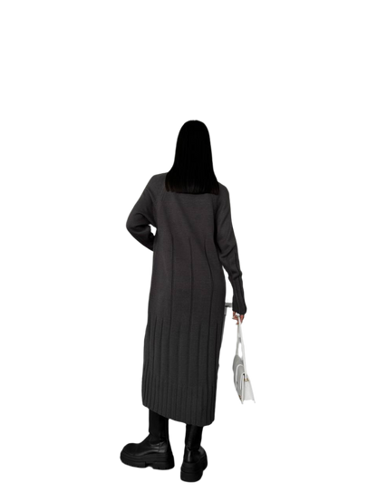 Person wearing a long dark coat holding a white bag on a white background