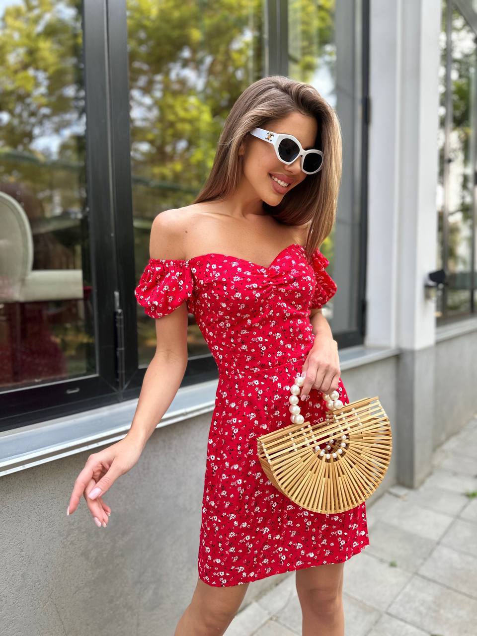Woman in a red floral dress holding a woven handbag outdoors.