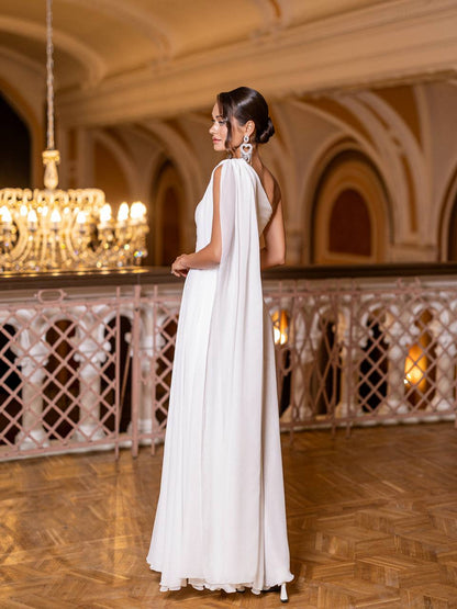 Woman in a white dress standing in an elegant indoor setting with chandeliers.