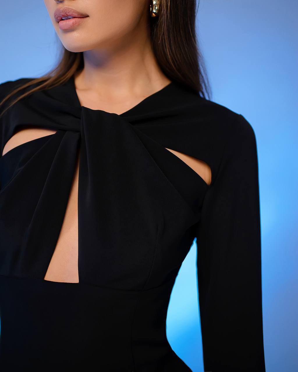 Black long-sleeve top with cut-out design on a blurred blue background