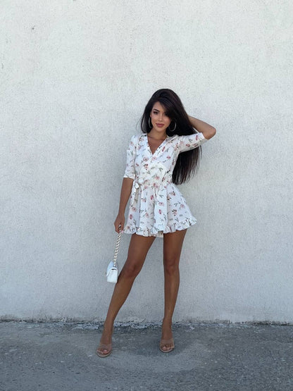 Woman in a floral dress standing against a plain wall
